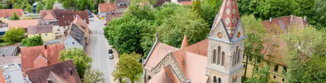 Bannerbild Luftaufnahme Mittig verläuft eine Straße rechts davon sieht man eine Kirche